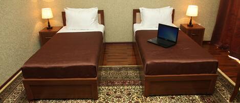 Habitación de hotel con dos camas, una computadora portátil sobre una de ellas, y piso alfombrado.
