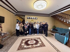 A group of people in a hotel lobby with a large patterned carpet, a staircase, and a reception desk. - Vardonze  (Bukhara)