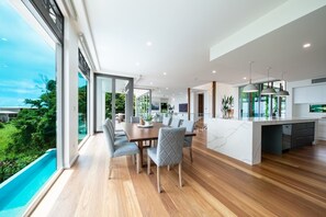 A modern kitchen with a marble island, large windows, and a dining area with a wooden table and chairs. - CoralAir Whitsundays (Airlie Beach)