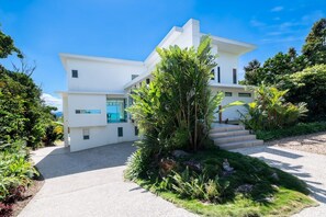 A modern two-story house with a white exterior, a visible staircase, and lush greenery surrounding the property. - CoralAir Whitsundays (Airlie Beach)