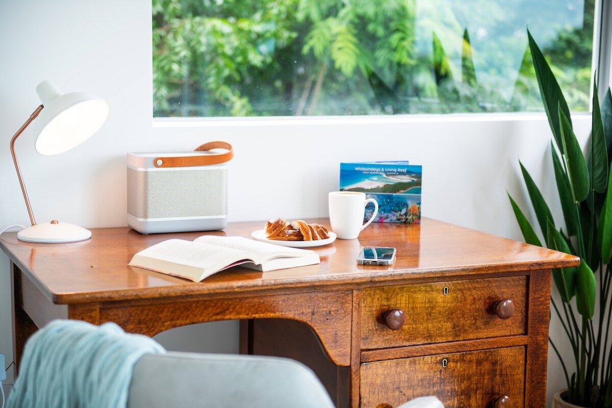 A wooden desk with a white lamp, a book, a mobile phone, a cup, and a book titled 'Whitsunday's & Living Reef'.