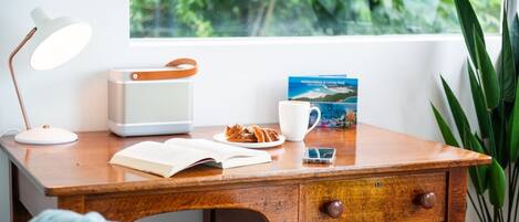A wooden desk with a white lamp, a book, a mobile phone, a cup, and a book titled 'Whitsunday's & Living Reef'.