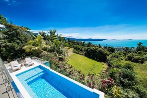 Una piscina con sillones de descanso, rodeada de exuberante vegetación y vistas al océano.