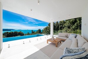 A modern living room with a large glass wall overlooking a pool and a scenic view. - CoralAir Whitsundays (Airlie Beach)