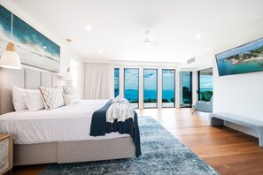 A modern bedroom with a large bed, a view of the sea through floor-to-ceiling windows, and a balcony. - CoralAir Whitsundays (Airlie Beach)