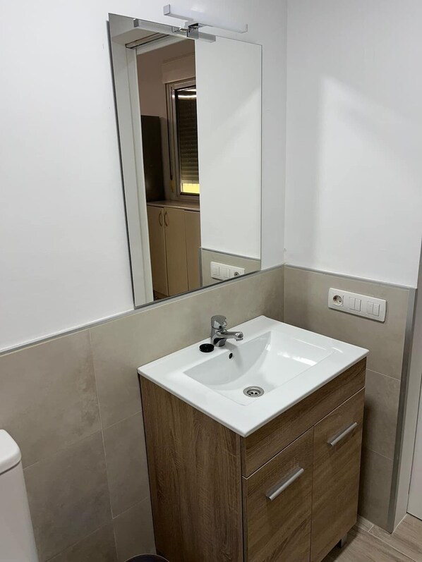 A bathroom with a white sink, wooden vanity, and a mirror.
