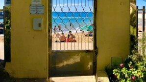 Une entrée fermée par un portail, offrant une vue sur une plage et l’océan.