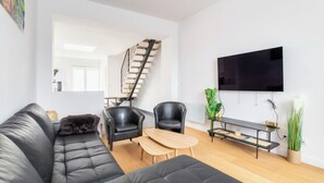 Una sala de estar moderna con un sofá de cuero negro, dos sillones de cuero negro, una mesa de centro de madera y un televisor montado en la pared.