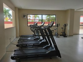 Uma academia com várias esteiras, uma bicicleta ergométrica e um ventilador na parede.