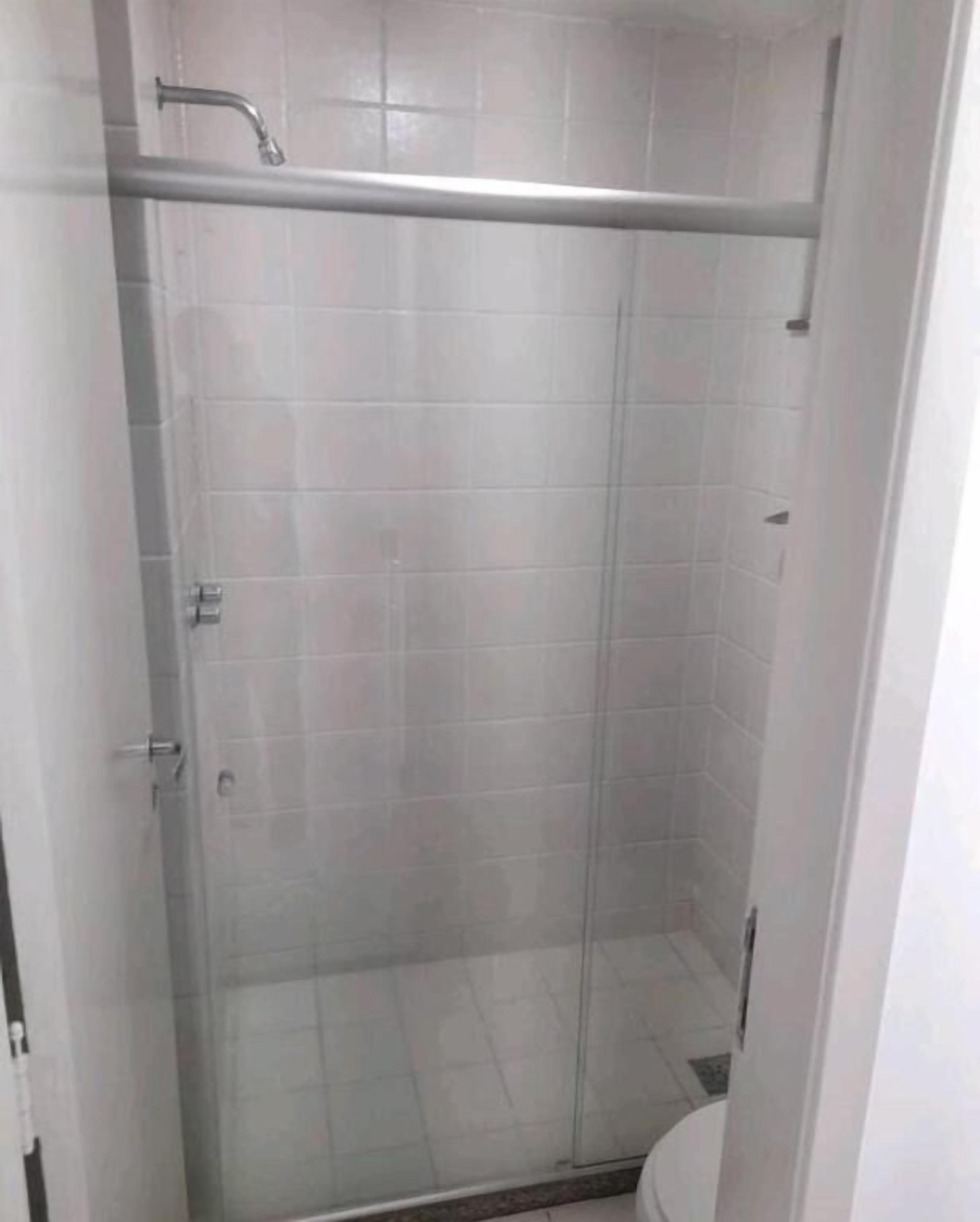 A small, enclosed shower stall with a glass door, tiled walls, and a metal handle.