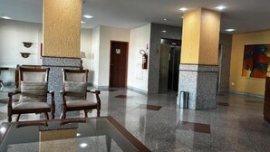 A lobby with a glass table, two wooden chairs, a fire extinguisher, and a door.