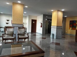Um hall com uma mesa de vidro, duas cadeiras de madeira, um extintor de incêndio e uma porta.