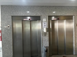 Dois elevadores com portas metálicas e um extintor de incêndio fixado na parede.