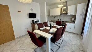 Een moderne keuken met witte kasten, een magnetron en een fornuis. Er is een eettafel met rode stoelen en een witte tafelkleed.
