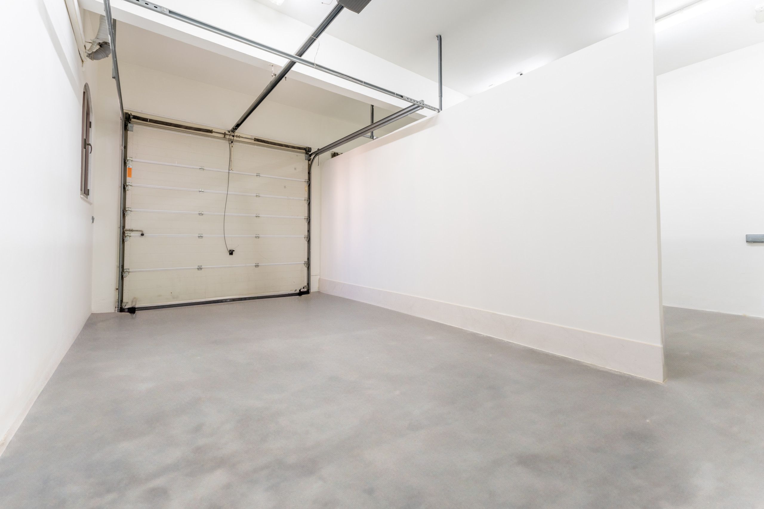 Een schone, lege kamer met een grijze vloer, witte wanden en een gesloten deur.