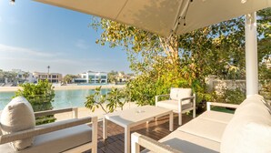 Ein überdachter Außenbereich mit weißer Möbel, mit Blick auf Pool und Strand.