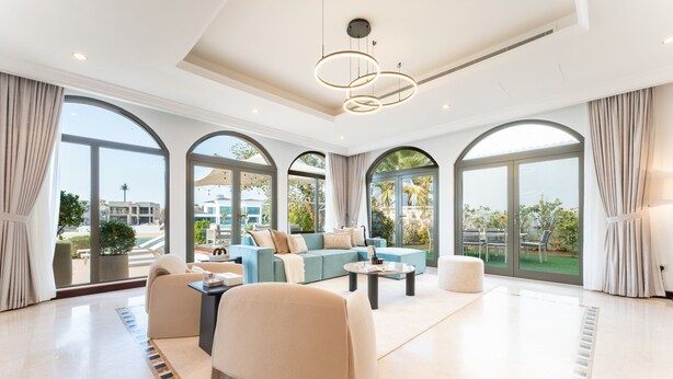 Ein geräumiges Wohnzimmer mit einer modernen Sofagarnitur, einem Couchtisch und einem großen Fenster mit Blick ins Freie.