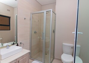 Een moderne badkamer met een douchecabine van glas, een wit wastafel en een toilet.