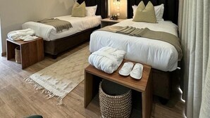Une chambre d’hôtel avec deux lits, une table de chevet avec des chaussons, une corbeille à déchets et un climatiseur fixé au mur.