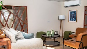 Un salon comprenant un canapé, un fauteuil vert, une table basse ronde et un lampadaire.