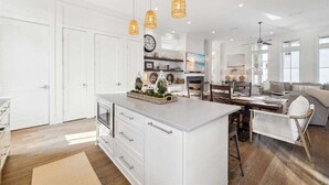 Una cucina spaziosa con mobili bianchi, un'isola centrale, illuminazione a sospensione e un'area pranzo con divano e sedie.
