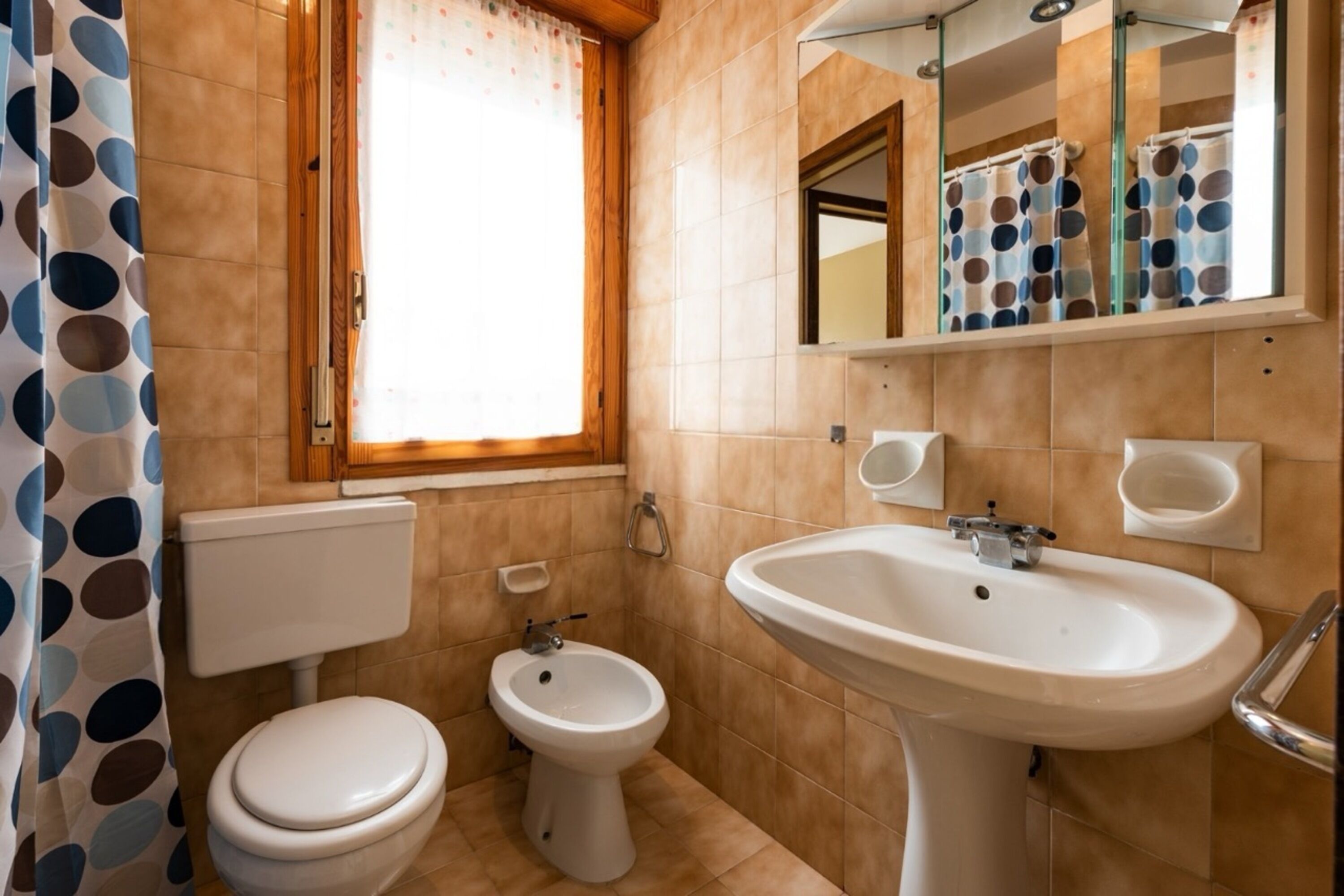 Un baño con inodoro, bidé, lavabo y una ventana con cortina.