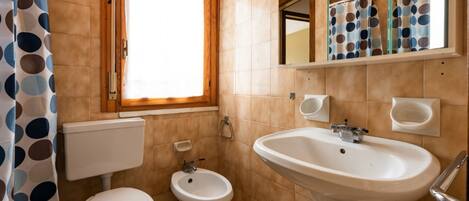 Un baño con inodoro, bidé, lavabo y una ventana con cortina.