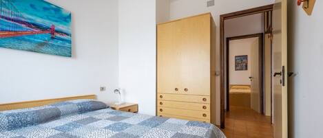 Un dormitorio con cama, un armario de madera, un cuadro de un puente y un pasillo que conduce a otra habitación.
