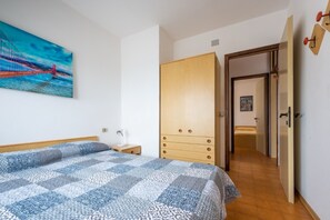 Ein Schlafzimmer mit einem Bett, einem Holzschrank, einem Gemälde einer Brücke und einem Flur, der in einen anderen Raum führt.