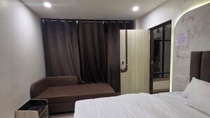 Una habitación de hotel con cama, sofá, control remoto y cortina.