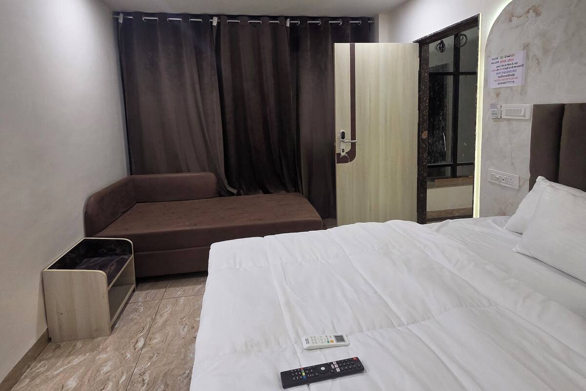 A hotel room with a bed, a sofa, a remote control, and a curtain.