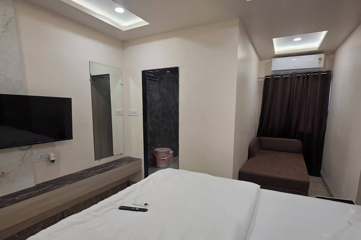 A hotel room with a bed, a ceiling fan, a TV mounted on the wall, and an air conditioning unit.
