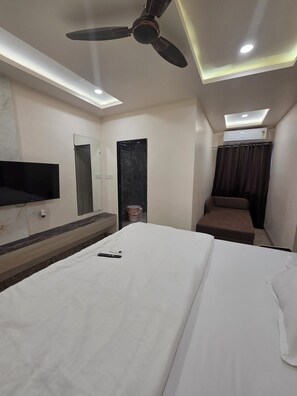 A hotel room with a bed, a ceiling fan, a TV mounted on the wall, and an air conditioning unit. - Kiwi Inn Hotel Regional Park (Indore)