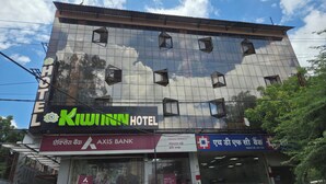 Un hotel con fachada moderna de vidrio, con un cartel visible que dice 'Kiwin Hotel' y una sucursal del banco 'Axis Bank' debajo.