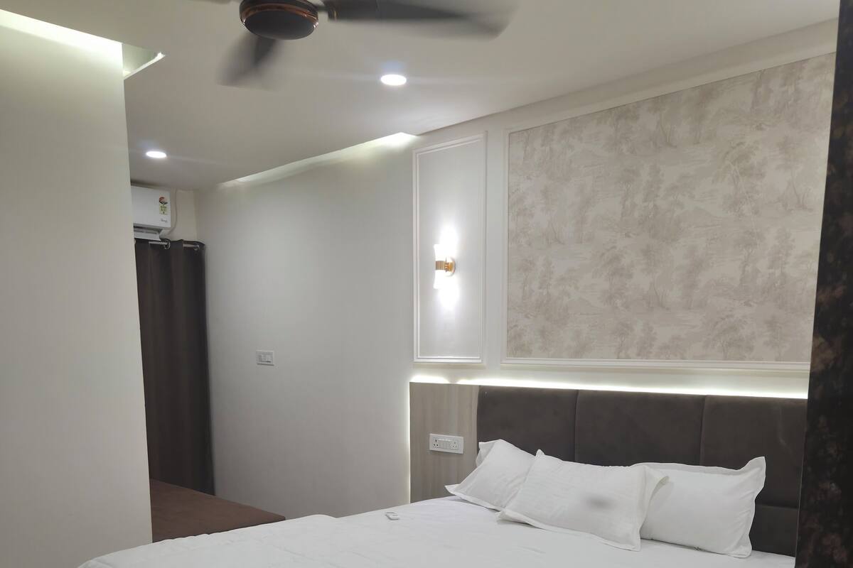 A modern bedroom with a large bed, a ceiling fan, recessed lighting, and a decorative wall panel.