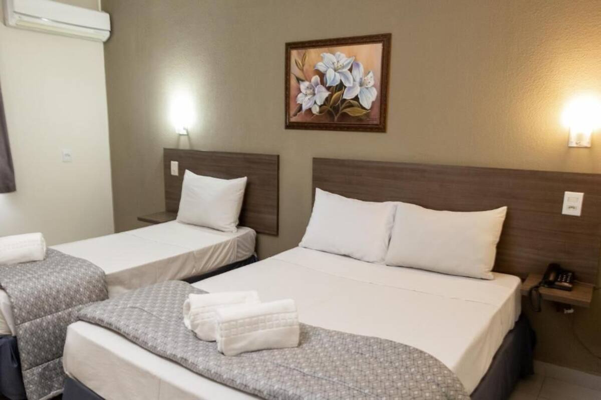 A hotel room with two single beds, a large bed, and a nightstand with a phone.
