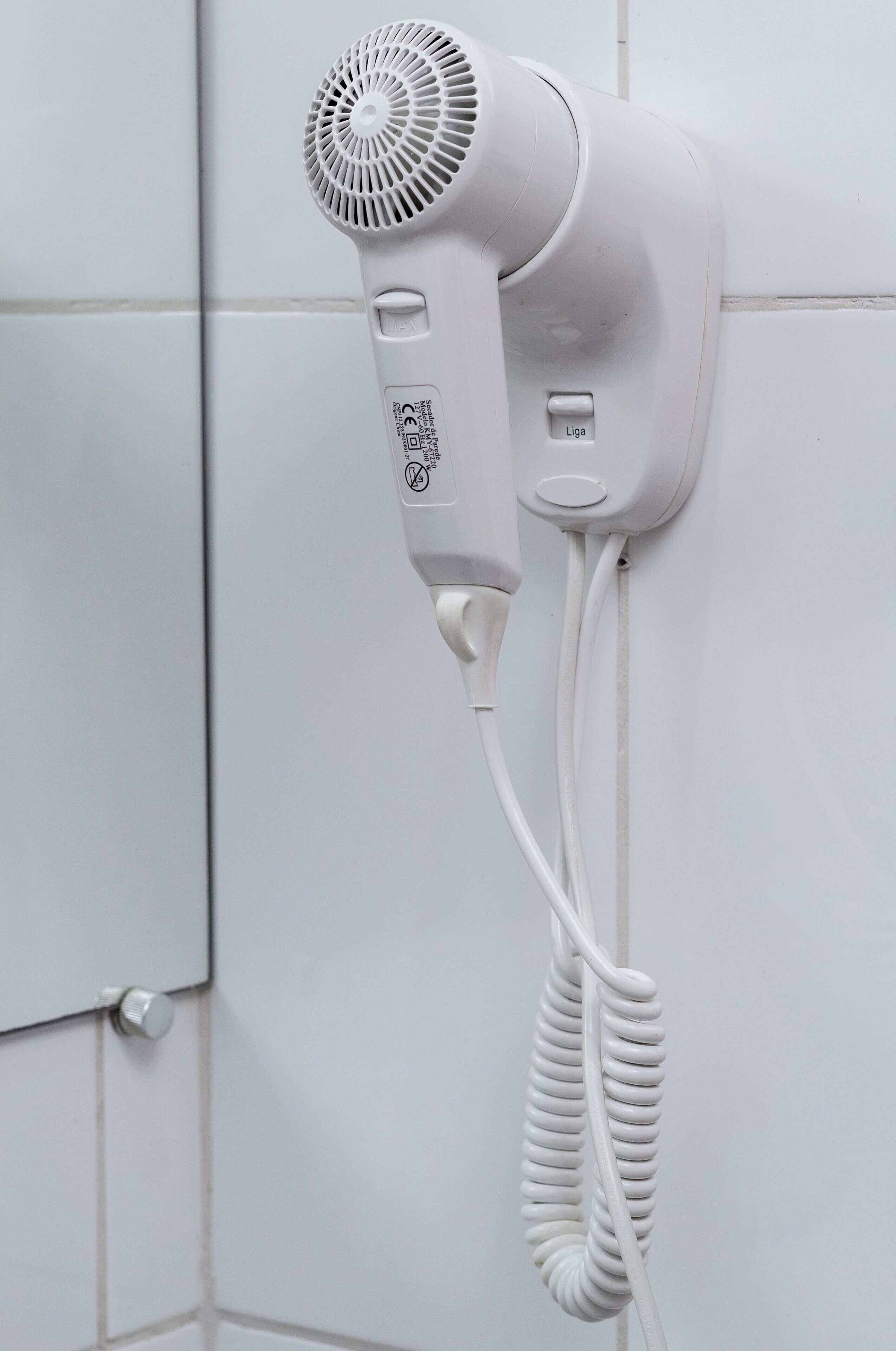 Un sèche-cheveux blanc fixé au mur, avec un cordon enroulé.