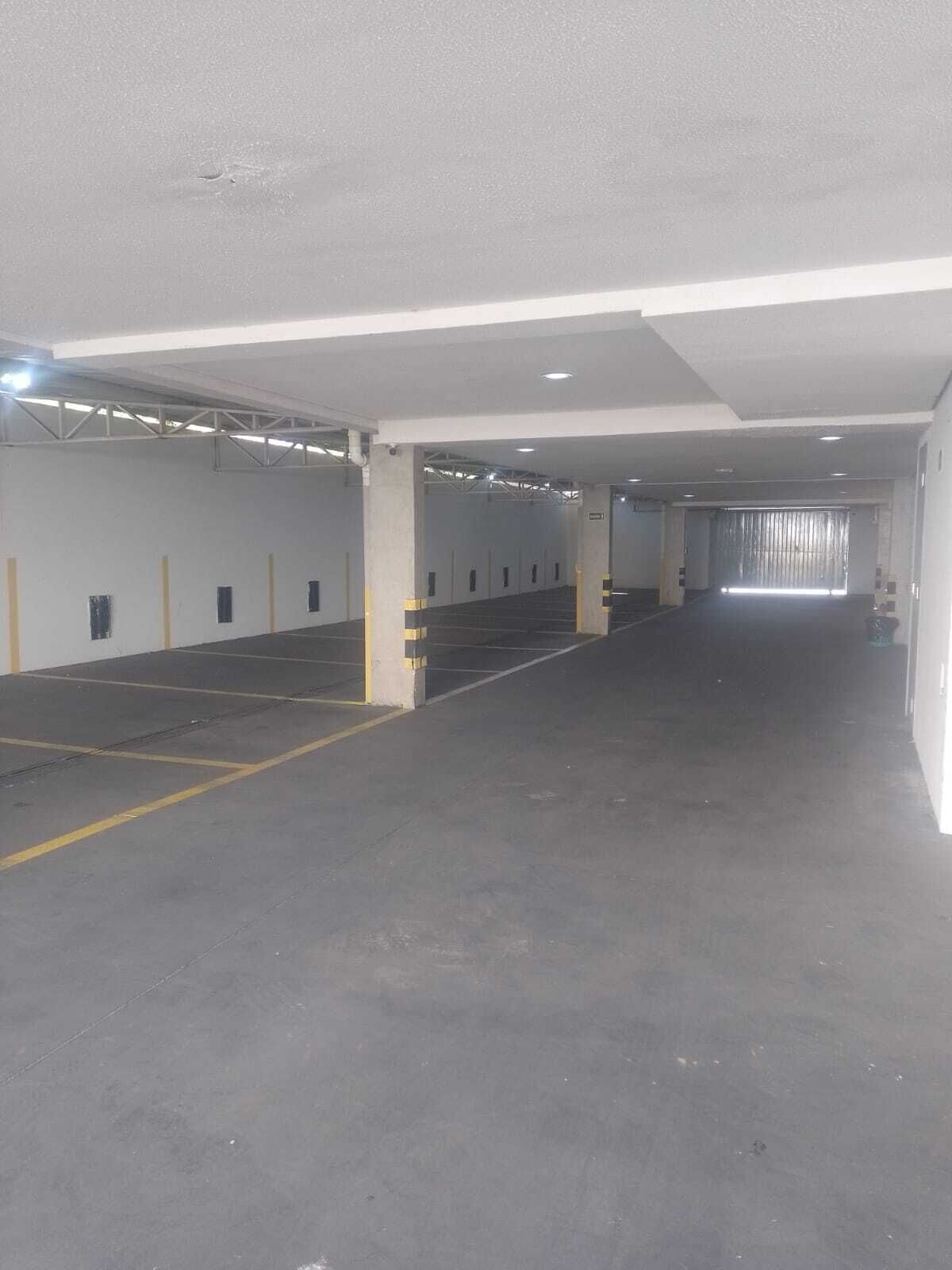 Un parking intérieur avec des planchers et des murs en béton, des emplacements de stationnement délimités et une allée centrale.