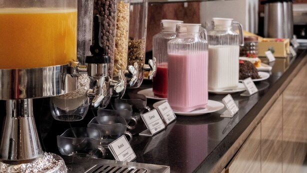 Una barra de desayuno con una máquina de café, diferentes recipientes de comida y una exhibición de frutas.
