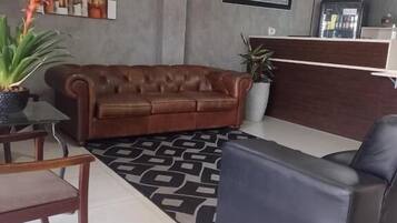 A modern reception area with a brown leather sofa, a black armchair, a reception desk, and a patterned rug.