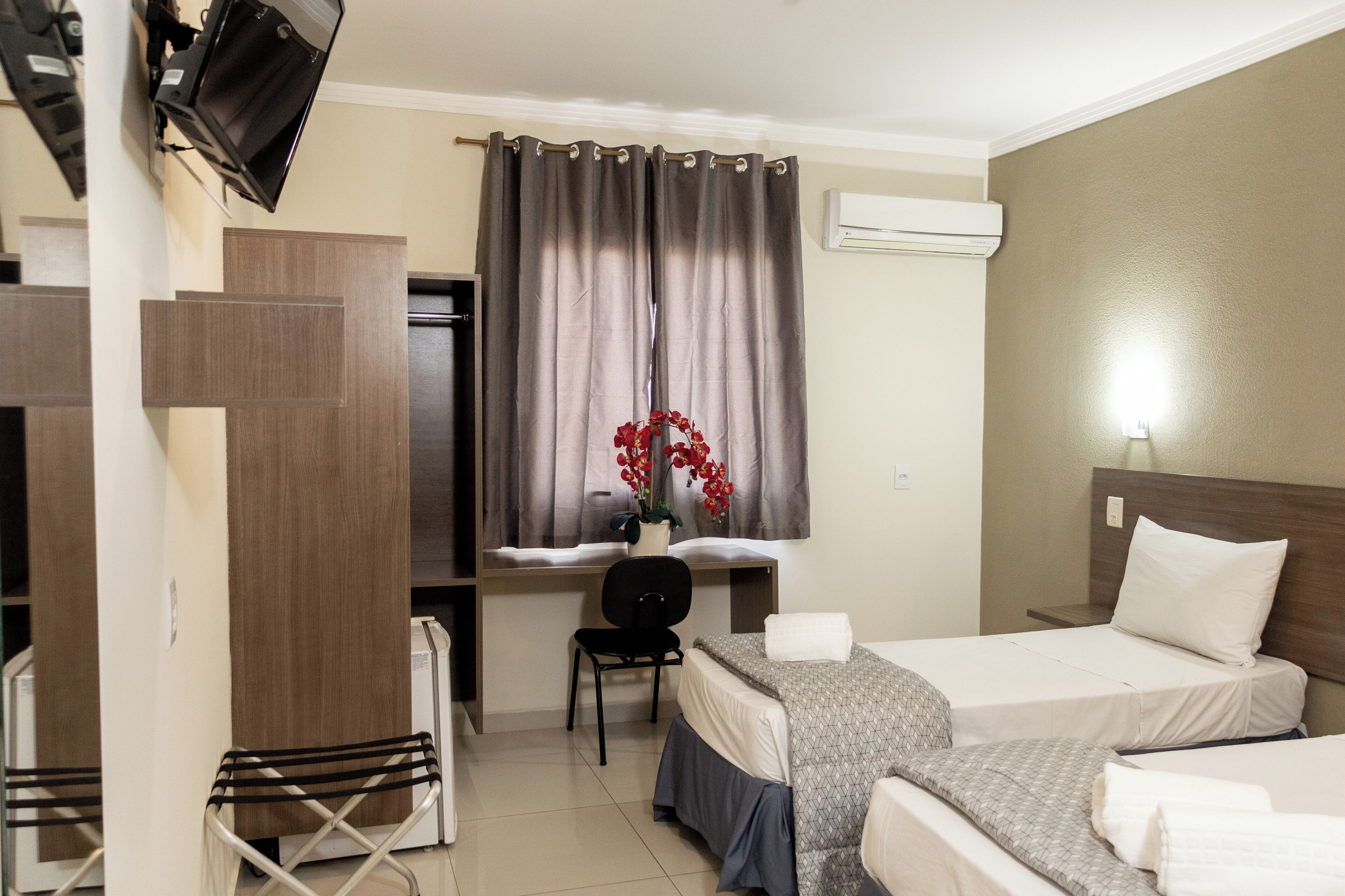 A hotel room with two beds, a desk, a chair, and an air conditioning unit.