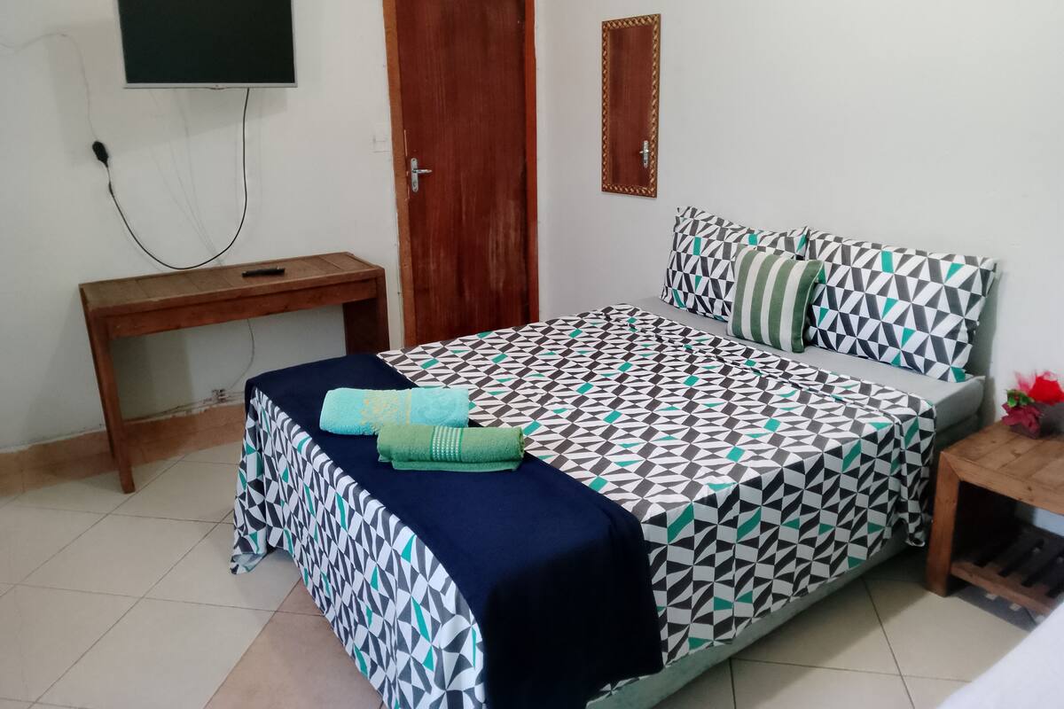 A bedroom with a bed, a desk, a TV mounted on the wall, and a door.