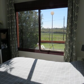 Ein Schlafzimmer mit großem Fenster, einem Bett und Blick auf einen eingezäunten Außenbereich.