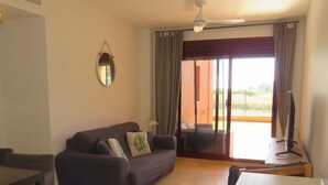 Een woonkamer met een bank, een eettafel, een televisie en een schuifdeur naar een buitenruimte.