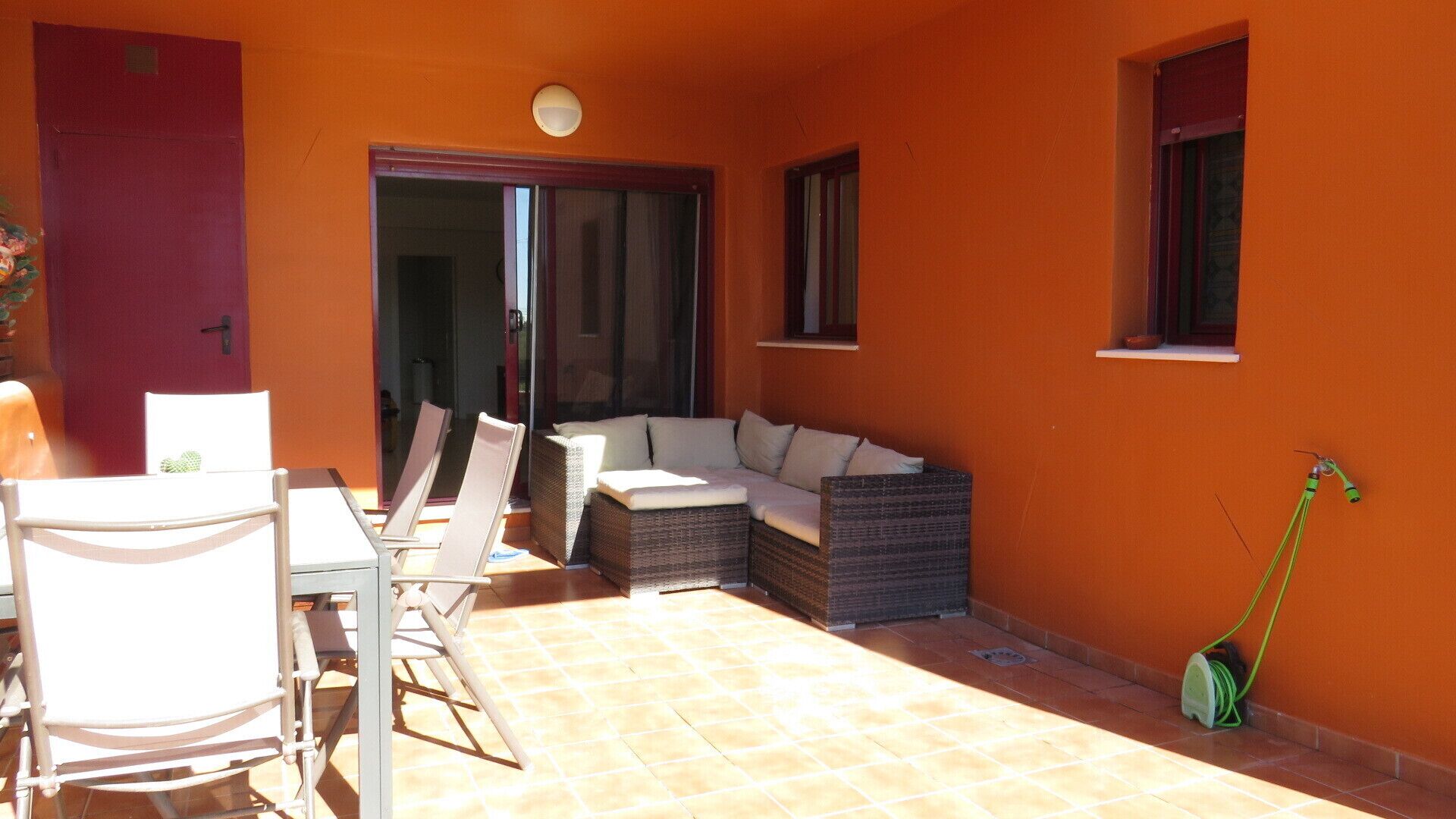 A sunlit patio with a dining table, chairs, a sofa, and a small garden hose.
