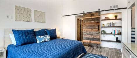 A bedroom with a large bed, a ceiling fan, a wooden wall panel, and a bookshelf with books and a plant.