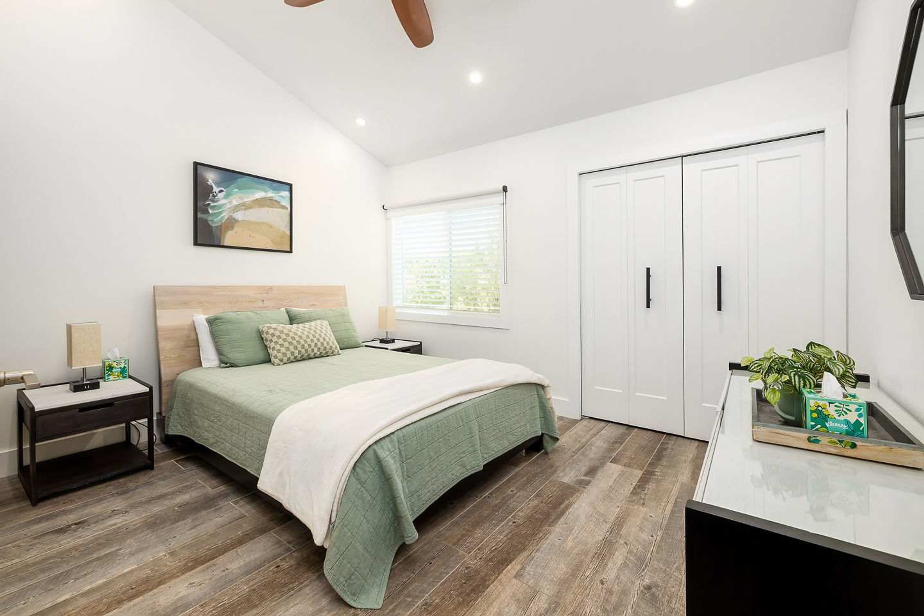 A bedroom with a bed, nightstand, bedside table, wardrobe, and a window with blinds.
