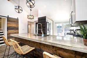 A modern kitchen with a large island, bar stools, and a potted plant. - Sea Bluff - Direct Beach Access (Encinitas)