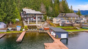 Une propriété située au bord de l’eau, dotée d’un quai, d’une grande maison avec balcon et d’un bâtiment plus petit avec un garage.