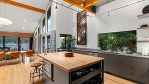 Une cuisine moderne dotée d’un îlot central, de planchers en bois et de grandes fenêtres donnant sur un plan d’eau.